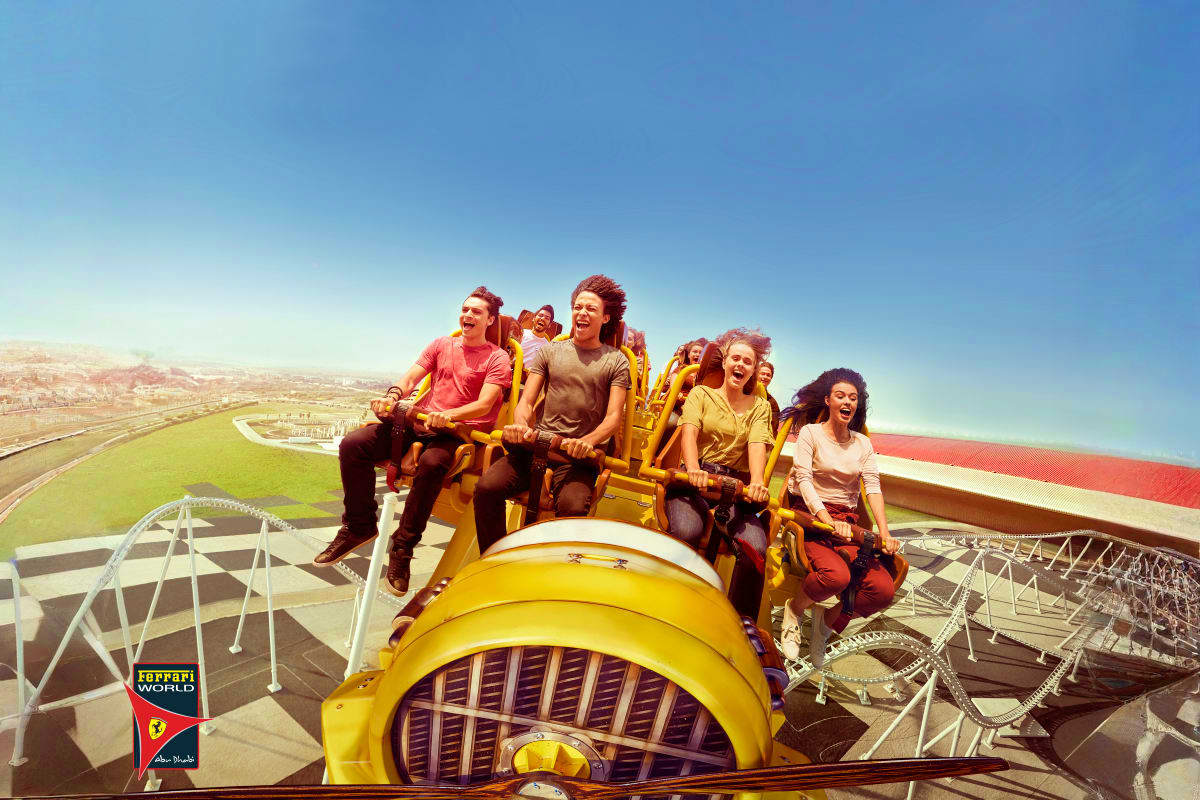 Group of visitors on yellow roller coaster ride at Ferrari World Abu Dhabi amusement park with cityscape view below