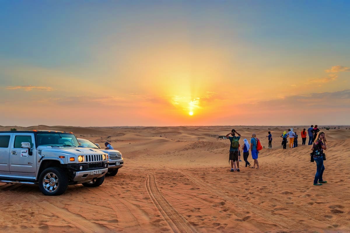 Group of tourists with SUV vehicle watching sunset in desert landscape during Abu Dhabi desert safari tour