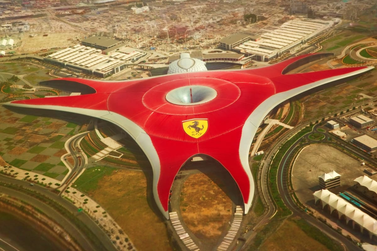 Abu Dhabi Stay And Play Luxury Package Aerial view of Ferrari World Abu Dhabi's distinctive red building with Ferrari logo and white roof structure surrounded by th