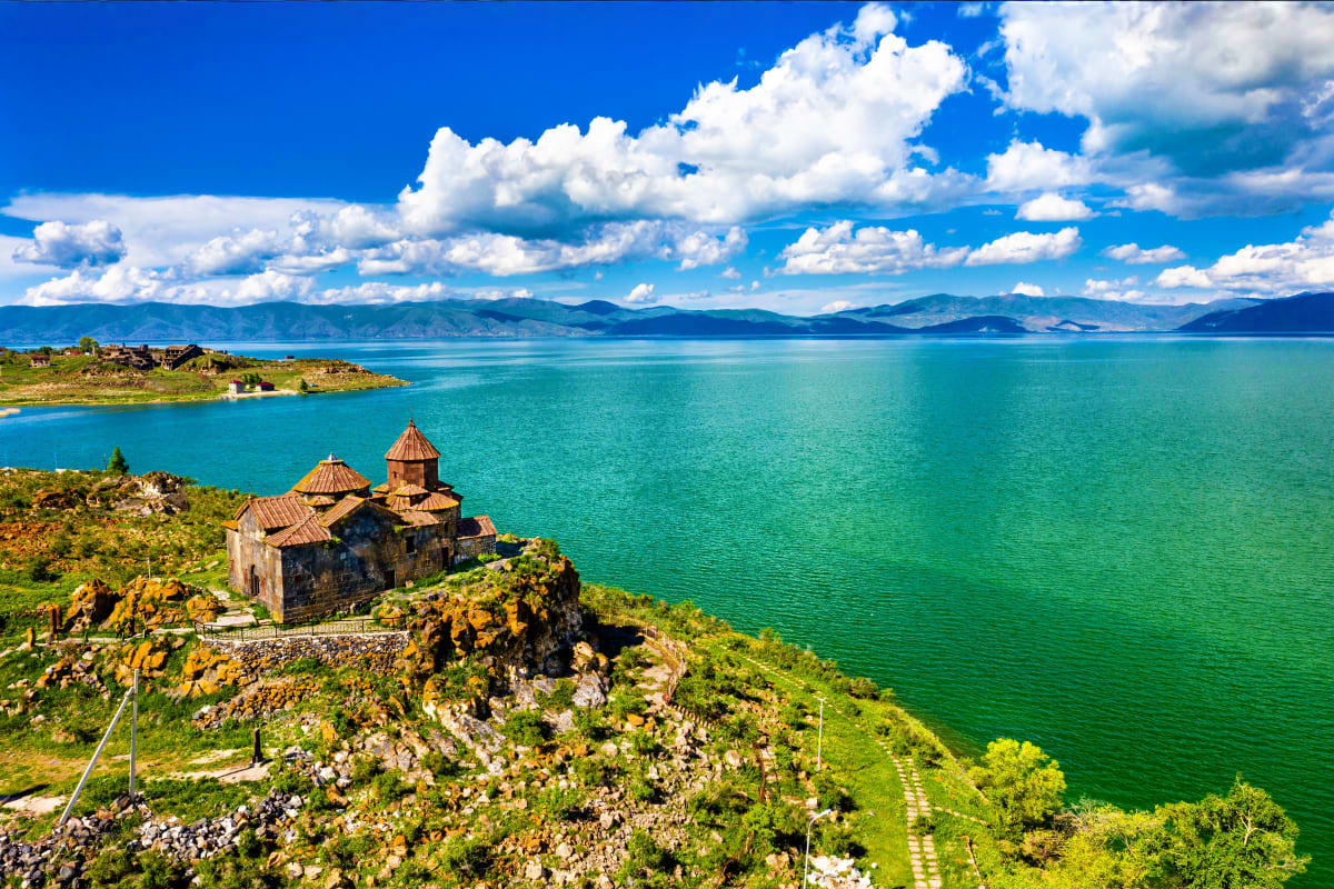 Akdamar Church sitting on a rocky peninsula in turquoise Lake Sevan, Armenia, with mountains and blue sky in background