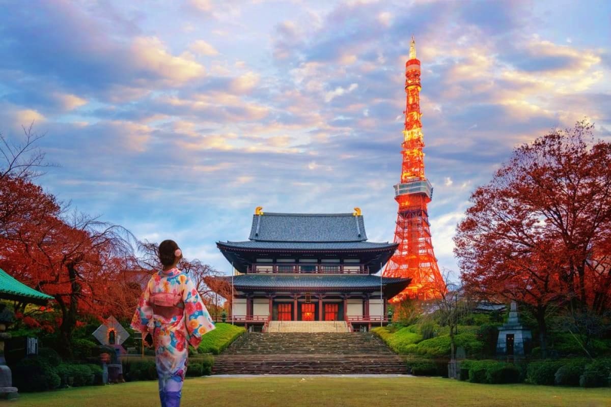 Woman in colorful kimono viewing illuminated red Tokyo Tower and traditional Japanese temple surrounded by autumn foliage at 