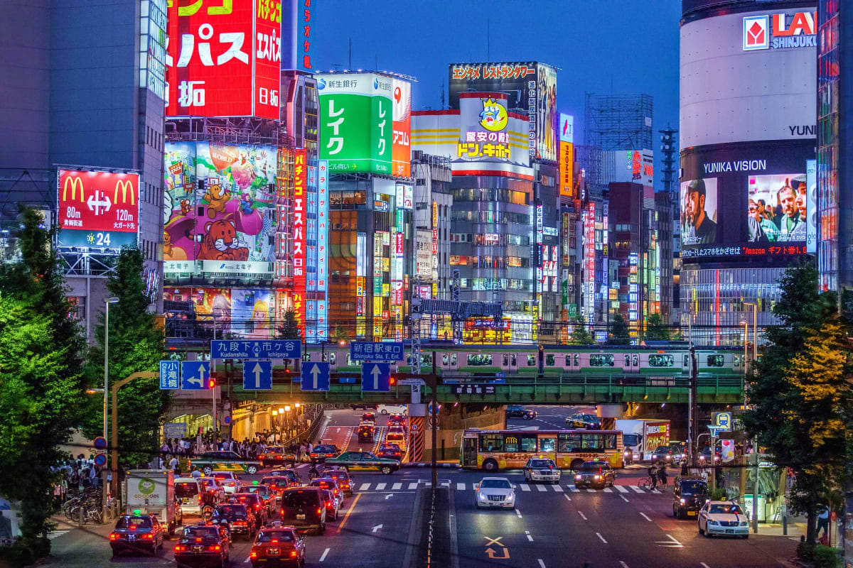 Shibuya Crossing at dusk with illuminated neon signs, buildings, train, and traffic in Tokyo, Japan