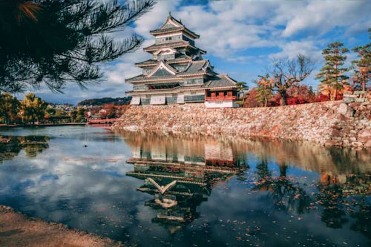Matsumoto Castle with white cherry blossoms and autumn foliage reflected in the moat water below