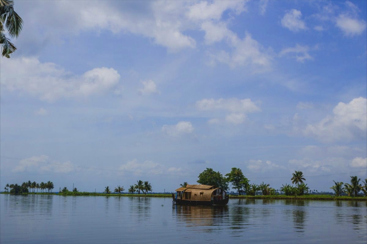 Traditional wooden houseboat floating on calm backwater with palm trees and blue sky in Kerala