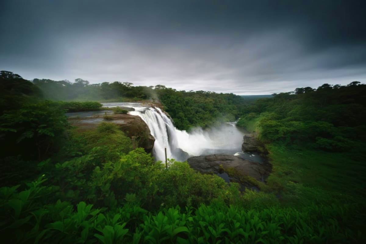 Waterfall cascading through dense green forest with mist and rainforest canopy under stormy sky