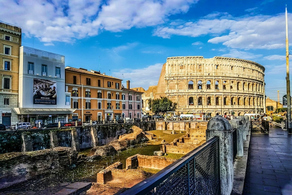 Colosseum and ancient Roman ruins in Rome, Italy, with surrounding historic buildings and blue sky