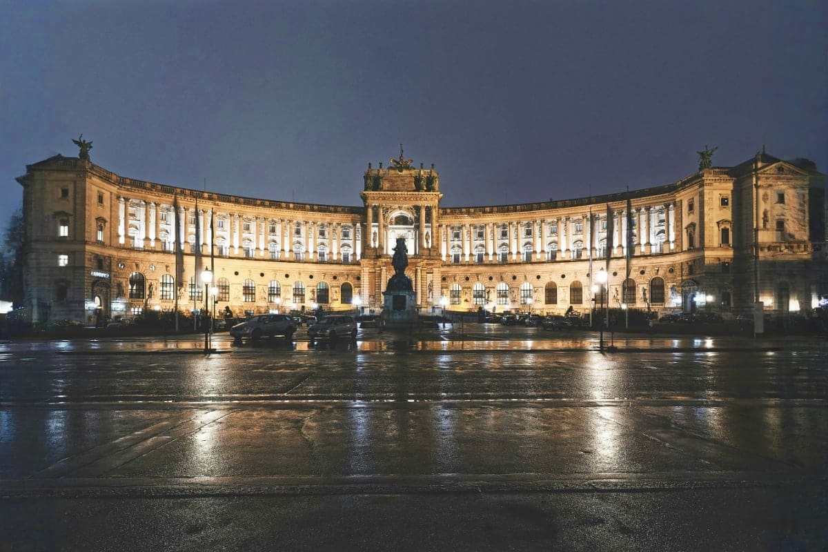 Hofburg Palace illuminated at night with wet plaza and equestrian statue in Vienna, Austria