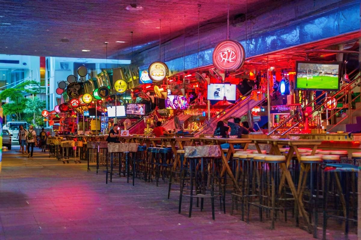 Modern sports bar with red neon lighting, hanging cookware decor, bar seating, and large screens displaying soccer match