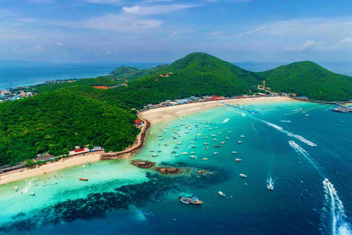 From Island Waves to City Wonders in Just 5 Days Aerial view of tropical island with turquoise waters, sandy beach, lush green hills, and traditional wooden boats anchored in