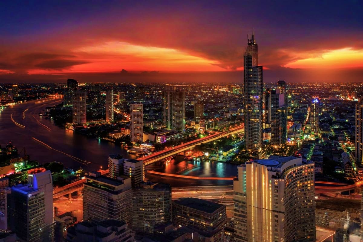 Bangkok cityscape at sunset with illuminated skyscrapers, Chao Phraya River, and glowing traffic lights reflecting on water