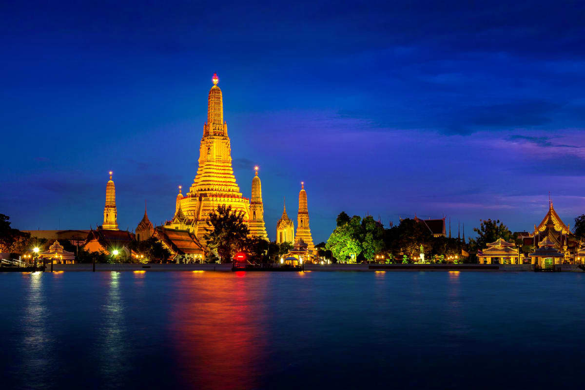 Wat Arun temple illuminated at dusk reflected in the Chao Phraya River in Bangkok, Thailand at twilight