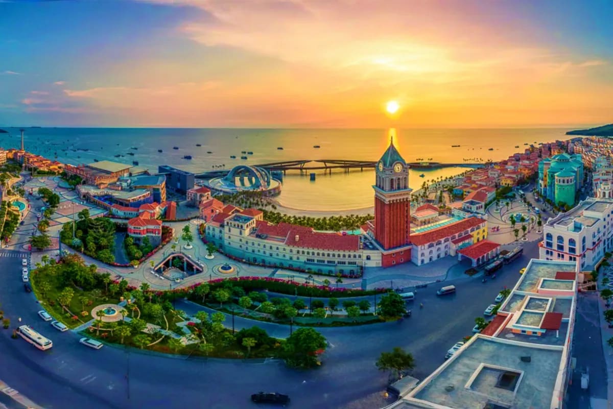 Halong Waves and Phu Quoc Days Aerial sunset view of a Vietnamese coastal resort with iconic bell tower, bay harbor dotted with boats, and colorful waterfro