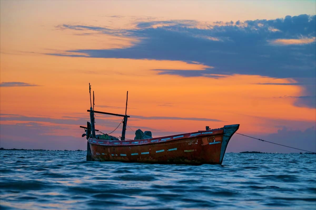 Mesmerizing Kerala Munnar to Kovalam Abandoned wooden fishing boat with two masts floating in calm ocean waters at sunset with orange and blue sky
