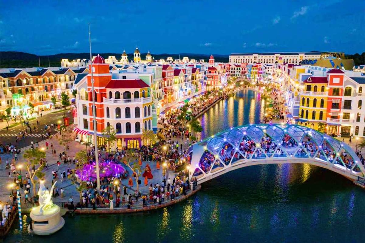 Aerial view of colorful waterfront buildings and a modern arched bridge over calm water at a tropical resort destination with