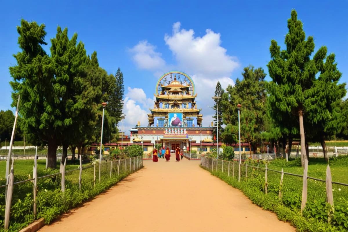 Buddhist monastery with golden dome and ornate architecture framed by cypress trees along dirt pathway in Karnataka
