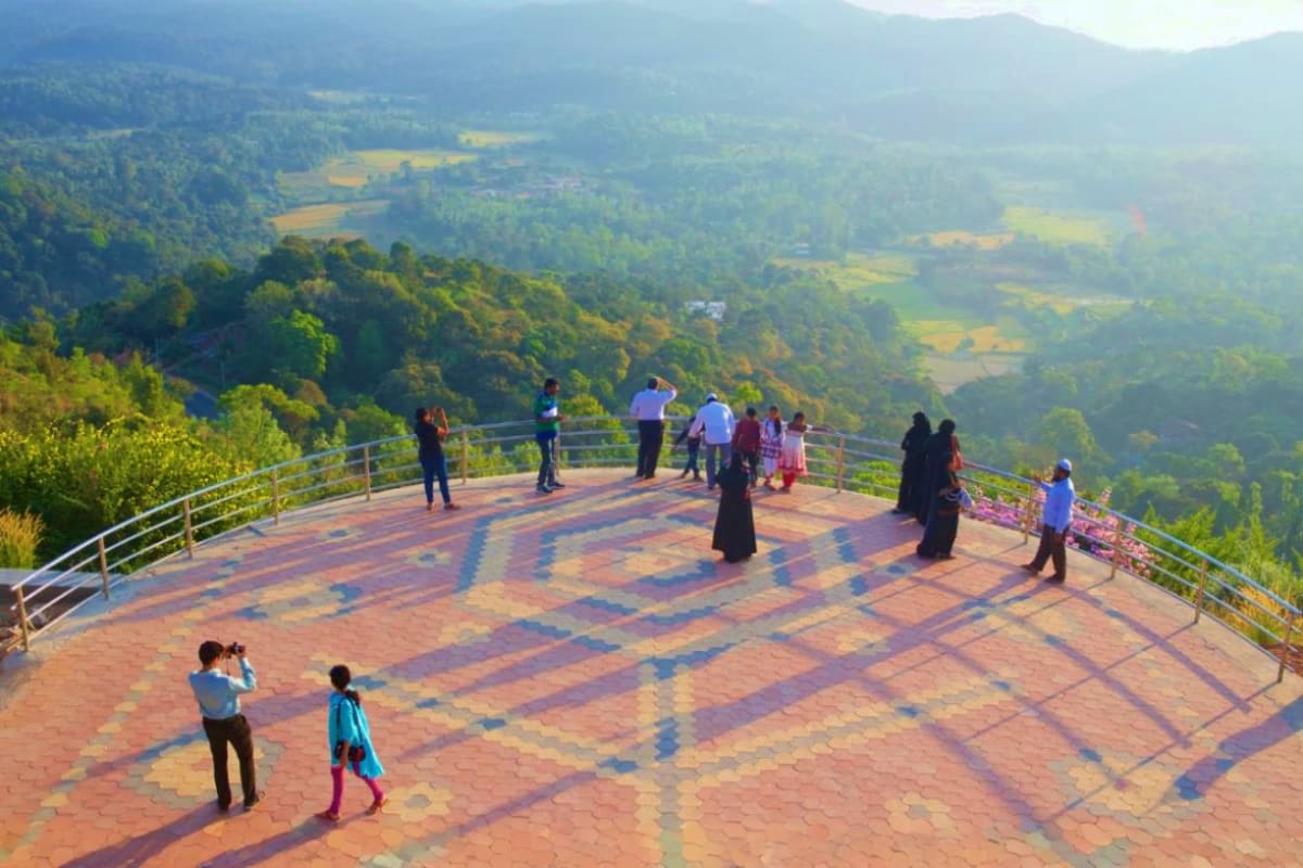 Tourists enjoying panoramic valley views from a brick observation deck with mountains and agricultural fields in the backgrou