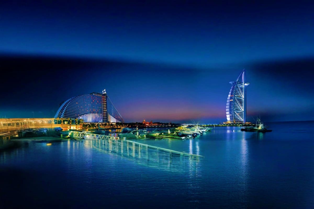 Burj Al Arab and Jumeirah Beach Hotel illuminated at twilight reflecting in calm Arabian Gulf waters in Dubai