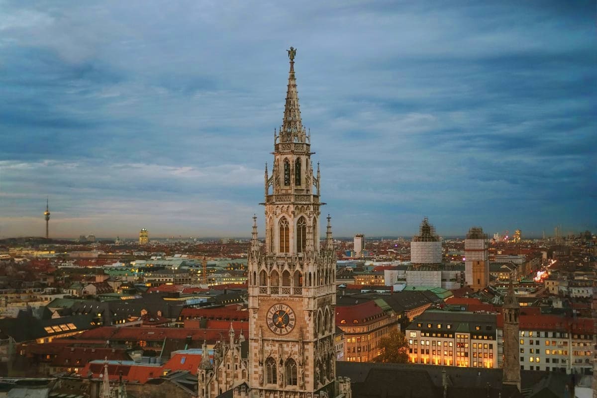 Munich cityscape at dusk with Neo-Gothic church tower and clock, illuminated historic buildings below