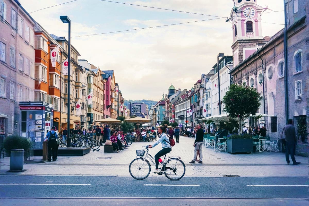 Three Capitals Woman riding bicycle on pedestrian street in European city with colorful historic buildings and clock tower
