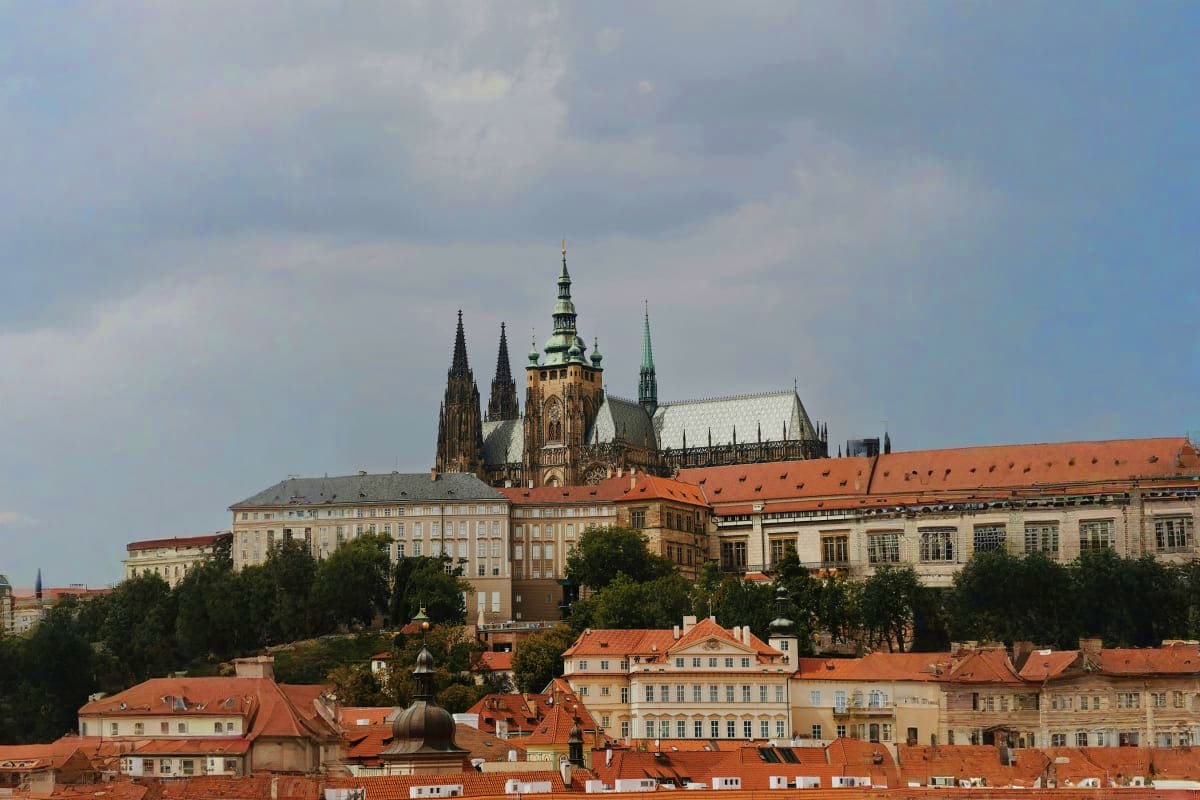 Prague skyline featuring St. Vitus Cathedral with Gothic spires towering above terracotta-roofed buildings and historic archi