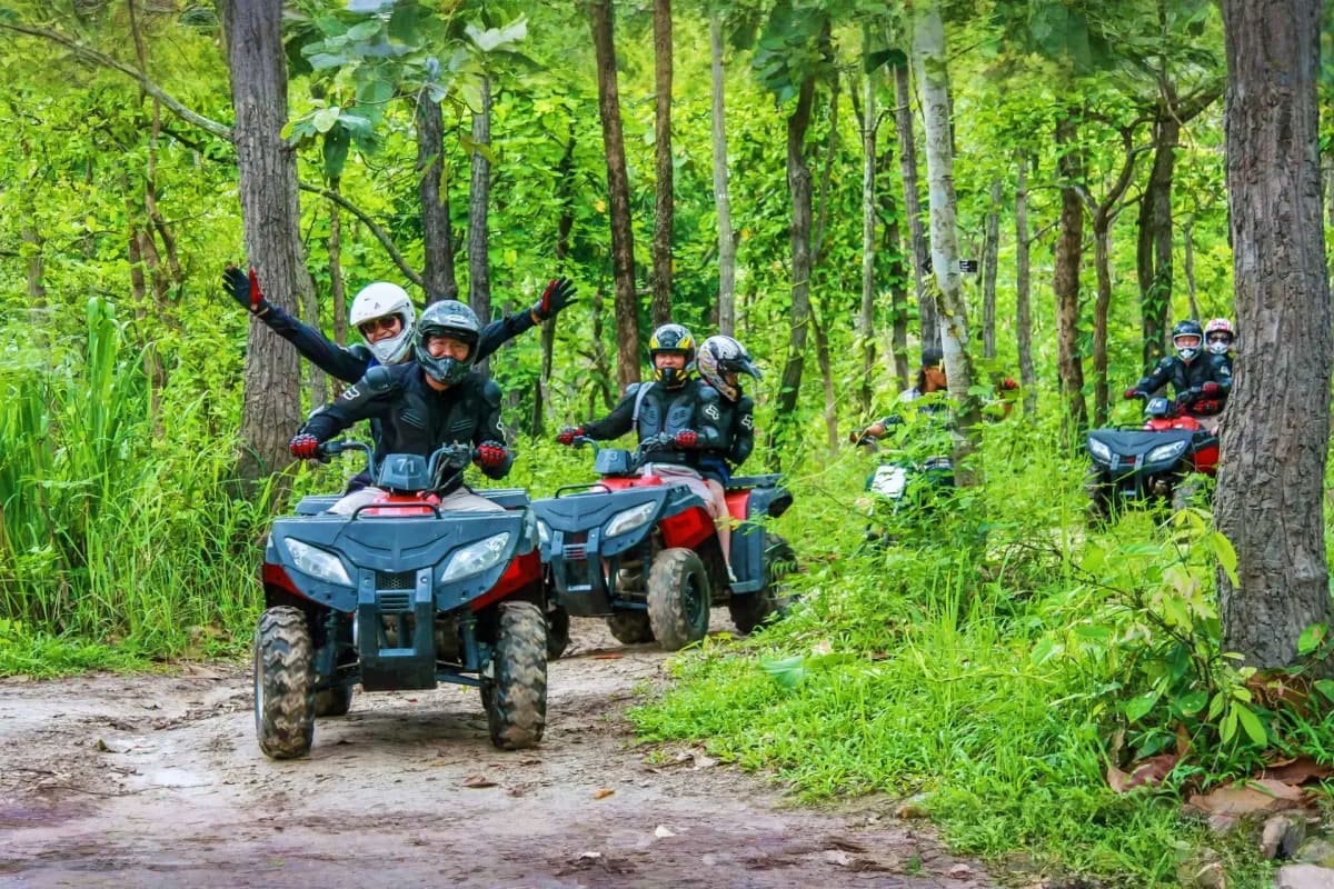 Exclusive Koh Samui Group of ATV riders on forest trail with helmets and safety gear, celebrating on red and blue quad bikes surrounded by trees