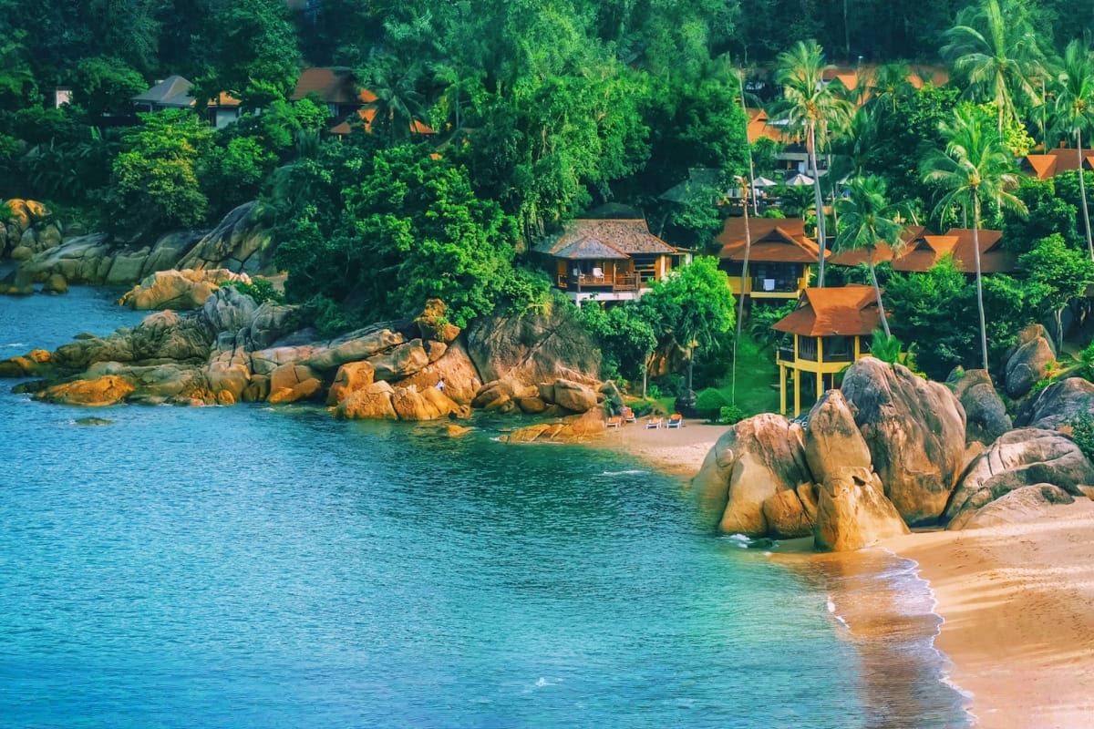 Exclusive Koh Samui Tropical beach resort nestled in lush jungle with golden granite boulders, turquoise waters, and wooden bungalows with orange