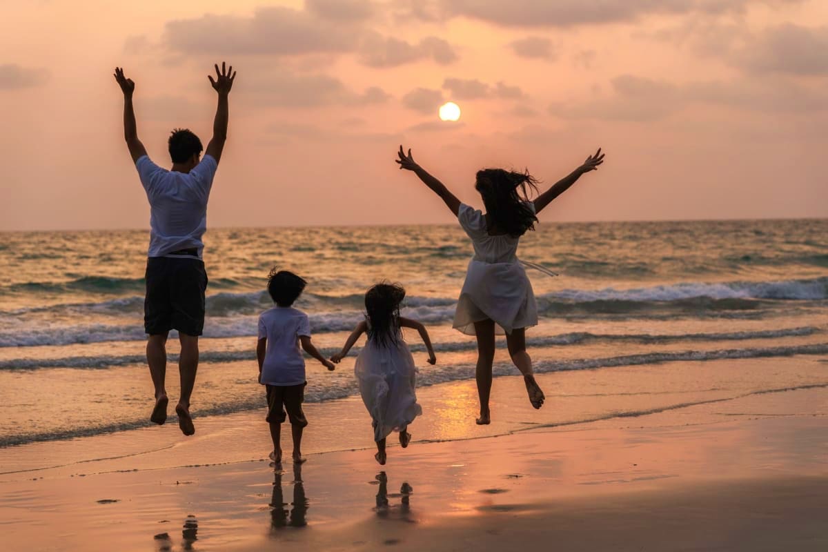 Exclusive Koh Samui Family of four jumping on beach at sunset with ocean waves and sun in background