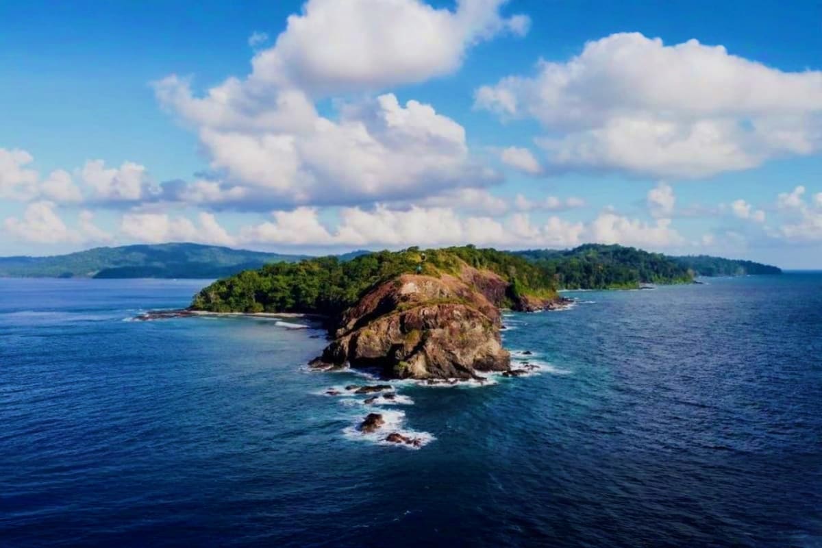 Tropical Port Blair Getaway 4 Days Island Experience Rocky forested island surrounded by blue ocean waters with white clouds and distant coastline under clear sky