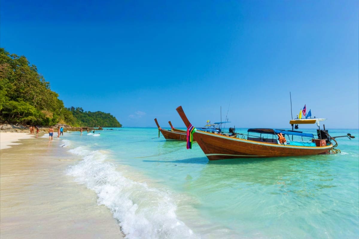 Tropical Port Blair Getaway 4 Days Island Experience Traditional wooden longtail boats anchored in turquoise water off a white sand beach with tourists swimming and tropical fore