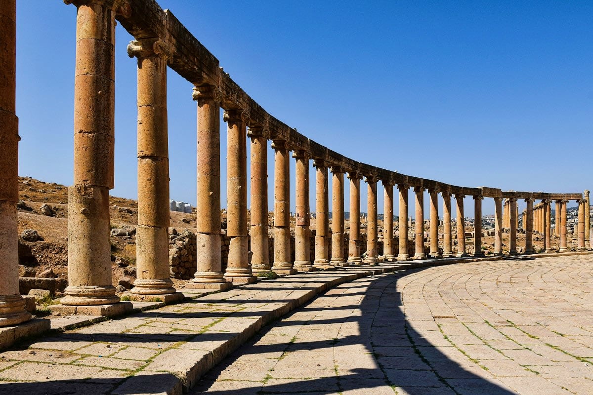 Ancient Roman columns lining a curved colonnade at Jerash archaeological site in Jordan under clear blue sky