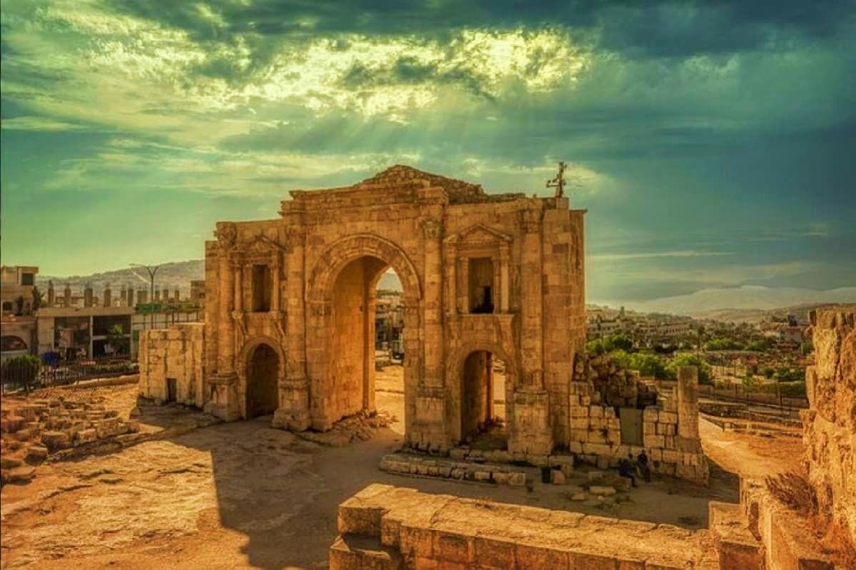 Ancient stone building with arches at Jerash archaeological site in Jordan, with desert landscape and mountains in background