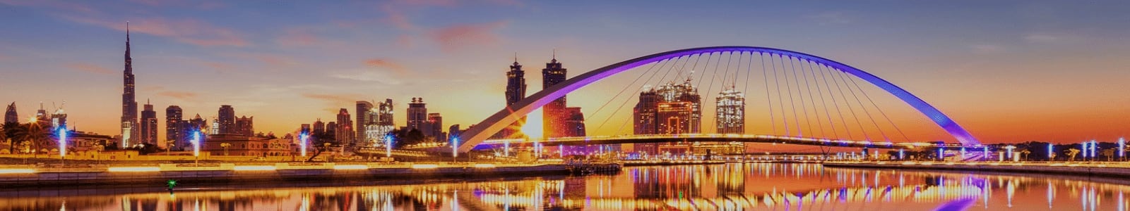 Dubai skyline at dusk with illuminated arch bridge reflected in still water