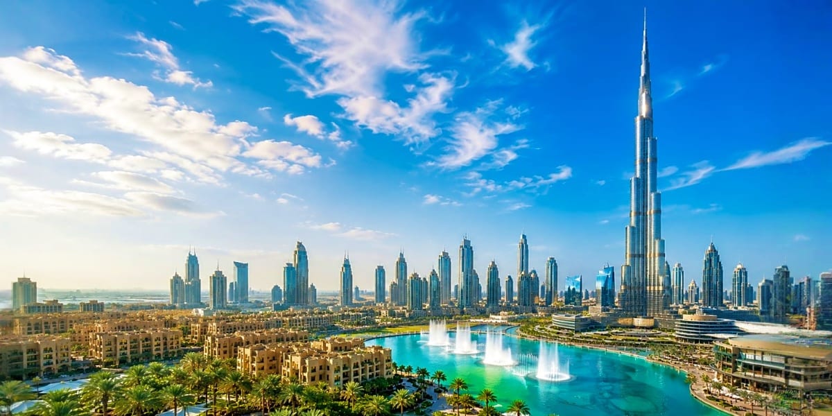 Dubai skyline with Burj Khalifa tower and turquoise Burj Lake fountain, surrounded by palm trees and modern buildings under b