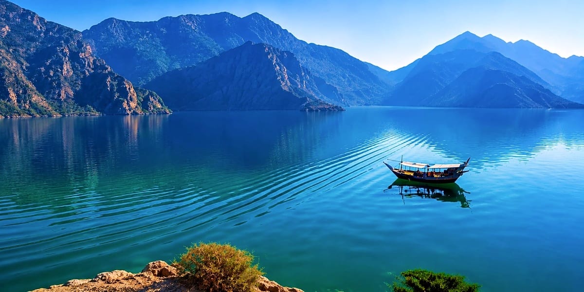 Wooden fishing boat on calm turquoise lake with dramatic rocky mountains in background under clear blue sky
