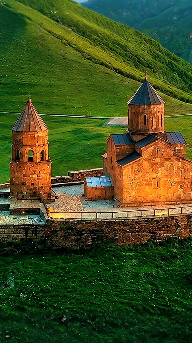 Armenian monastery with red stone buildings and conical domes in lush green valley surrounded by mountains, Georgia