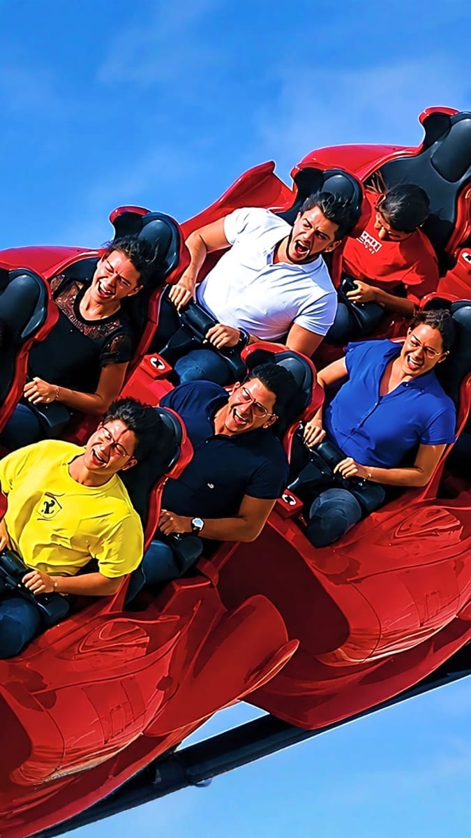 Group of excited riders on a red roller coaster against a blue sky at an Abu Dhabi amusement park