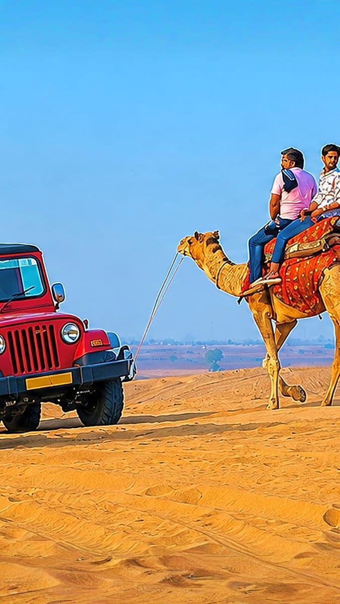 Two tourists riding a decorated camel in Jaisalmer desert being towed by a red jeep under clear blue sky