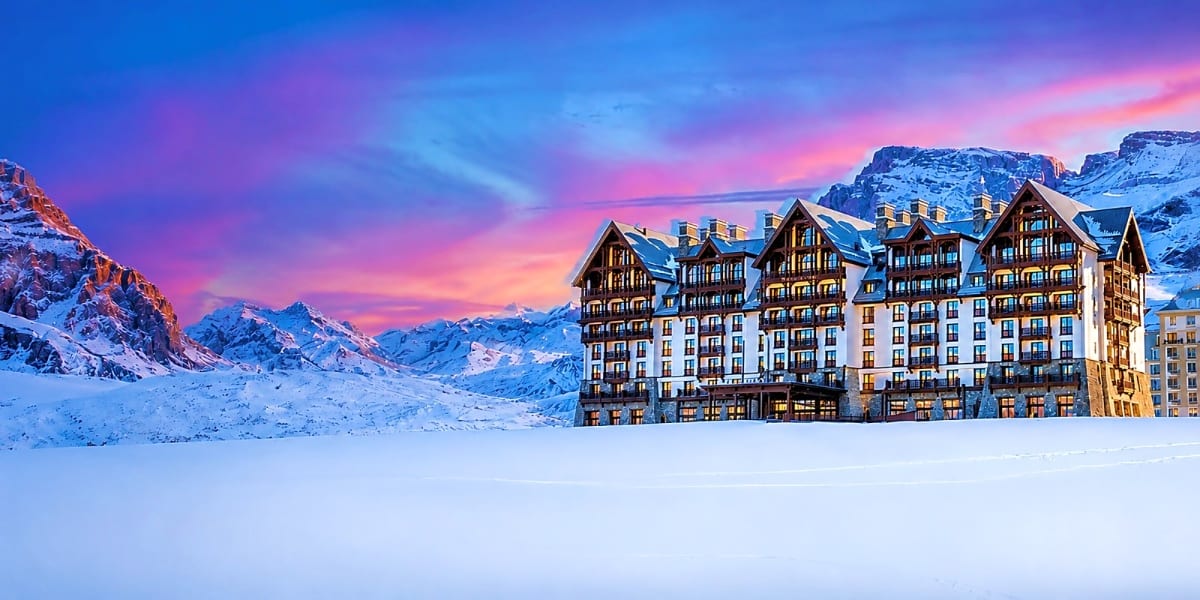 Luxury alpine resort hotel with illuminated windows surrounded by snow-covered mountains at sunset in Azerbaijan