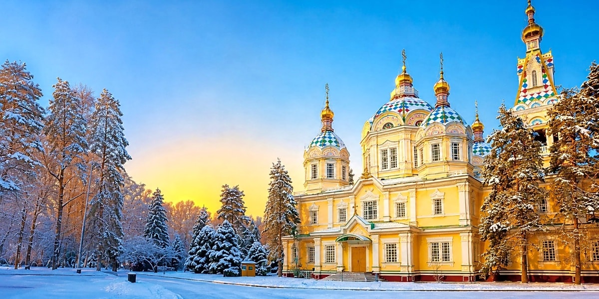 Yellow Orthodox cathedral with golden domes surrounded by snow-covered pine forest in winter landscape