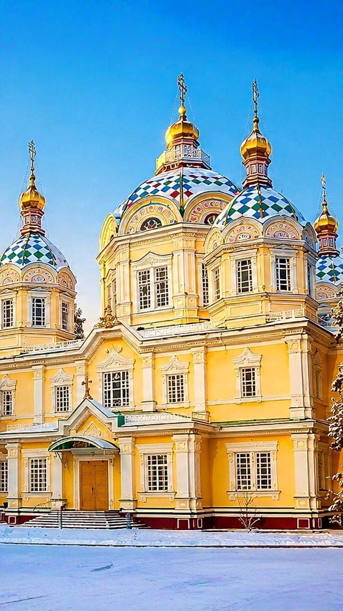 Yellow Orthodox cathedral with golden domes and blue diamond patterns in snow-covered landscape under clear blue sky