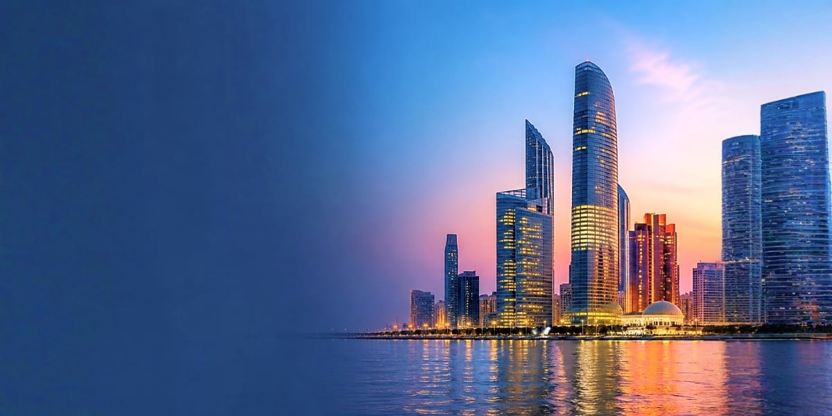 Abu Dhabi waterfront skyline at dusk with illuminated high-rise buildings reflected in calm harbor water