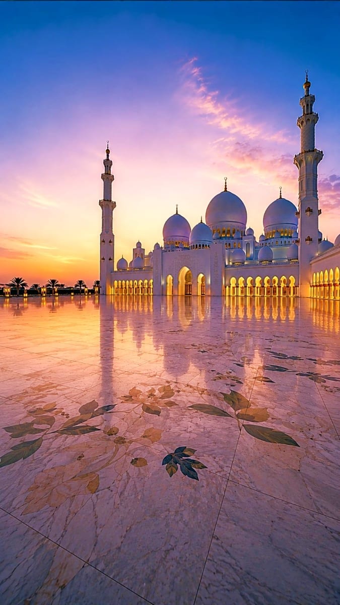 Sheikh Zayed Grand Mosque at sunset in Abu Dhabi, with illuminated white domes, minarets, and reflective courtyard at dusk
