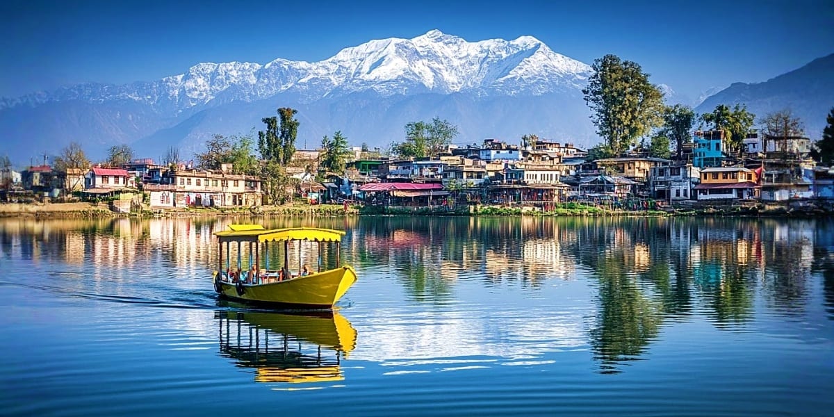 Yellow traditional shikara boat on Dal Lake with snow-capped mountains and colorful waterfront buildings in Srinagar, Kashmir