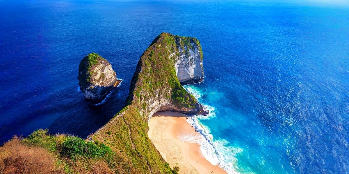 Aerial view of Kelingking Beach cliffs in Bali with turquoise ocean, sandy cove, and distinctive rock formations