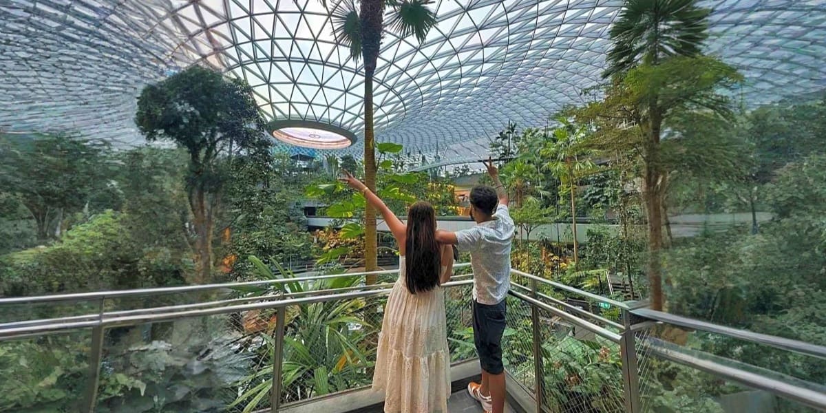 Couple pointing upward inside a glass-domed tropical conservatory with lush greenery and palm trees at Sentosa Island