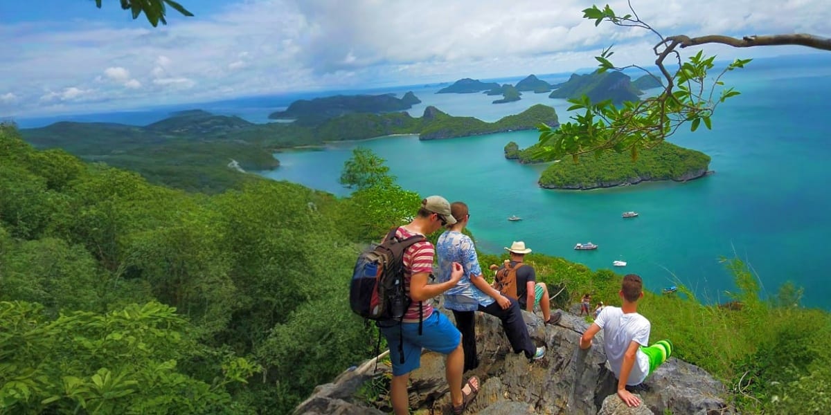Hikers viewing turquoise waters and forested islands in Koh Samui archipelago from rocky mountain overlook