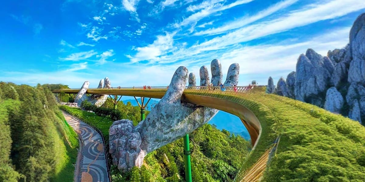 Golden Bridge held by giant stone hands in lush green landscape with blue sky and tourists walking across