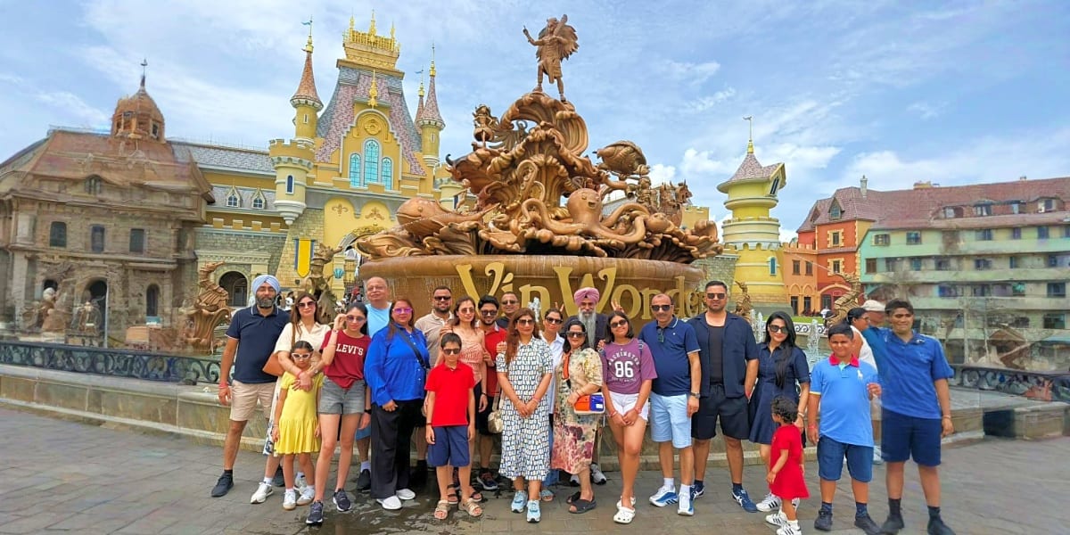 Large group of tourists posing in front of golden statue and ornate temples with yellow spires in Southeast Asian temple comp