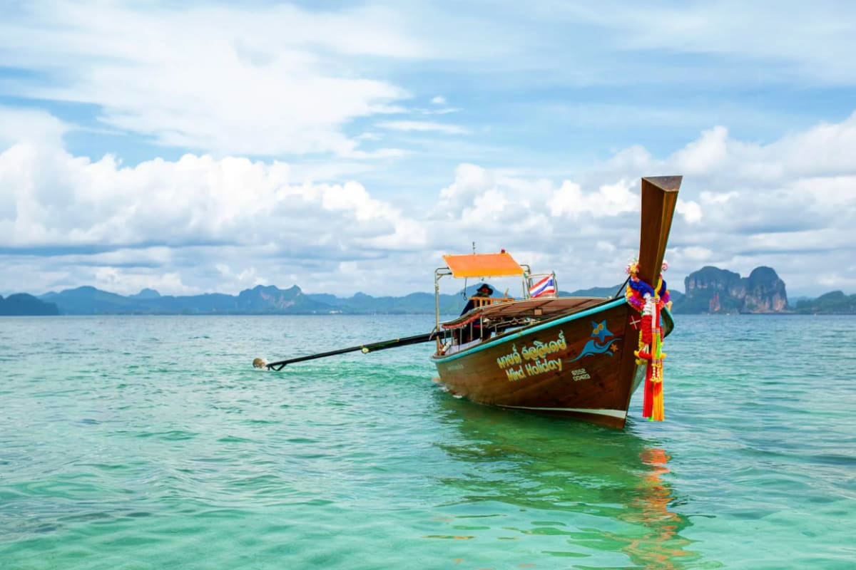 Traditional wooden long tail boat with orange canopy anchored in turquoise waters, limestone karst mountains in background, T
