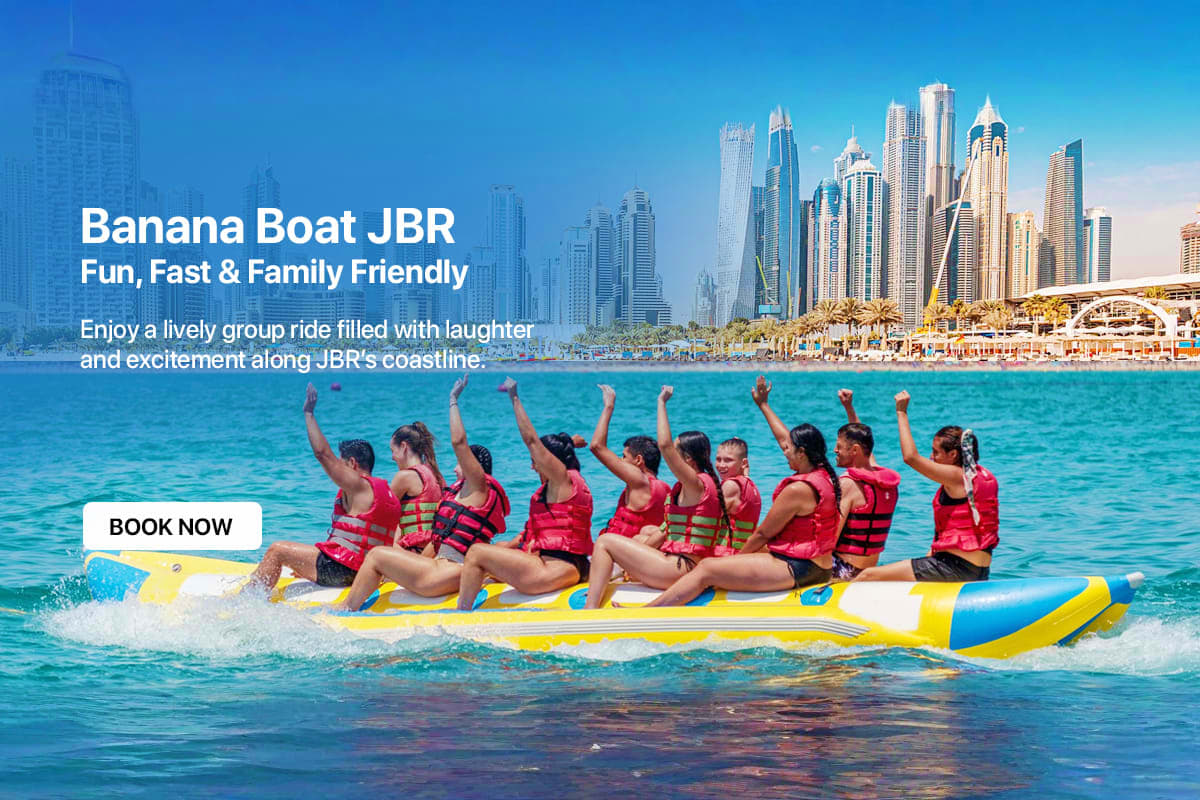 Banana Boat Ride in Dubai 15 Min Group of people riding yellow and blue banana boat with raised arms in turquoise water off Dubai beach with marina skyline in